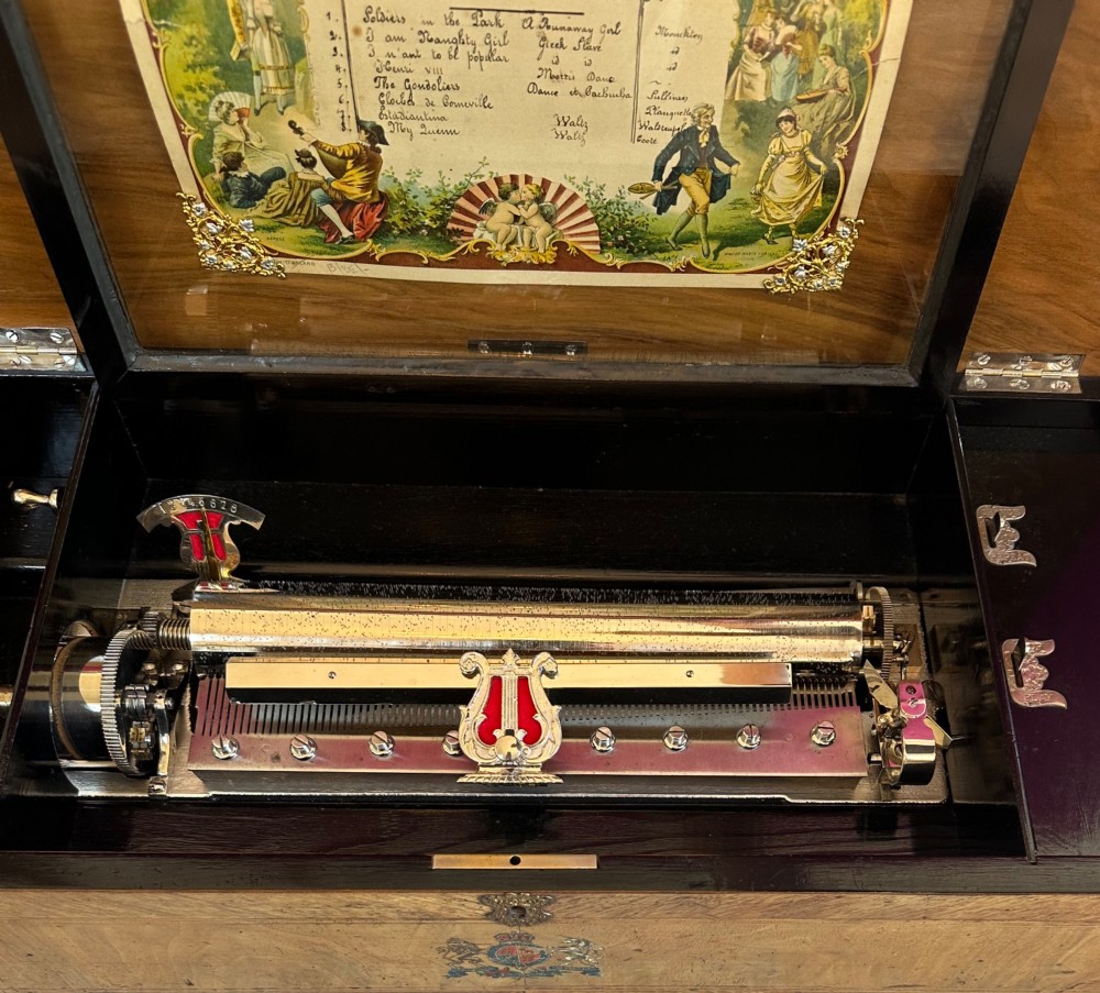 A late nineteenth-century Victorian walnut cylinder music box with an open hinged lid displaying an illustrated tune sheet and an internal brass mechanism behind a glass cover. View V