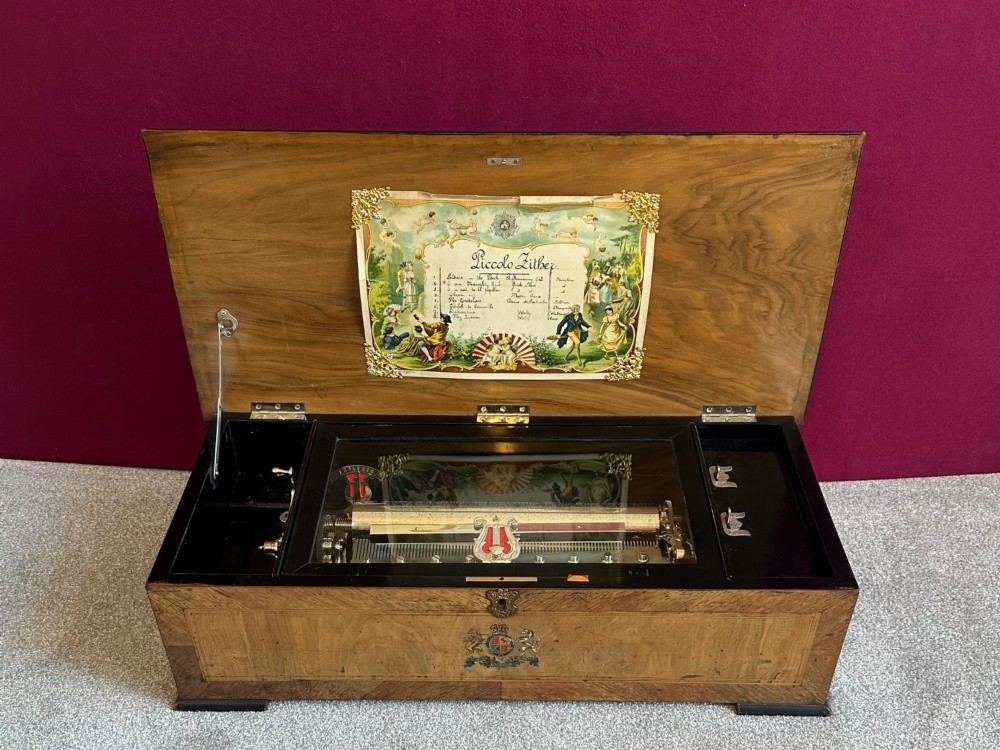 A late nineteenth-century Victorian walnut cylinder music box with an open hinged lid displaying an illustrated tune sheet and an internal brass mechanism behind a glass cover.