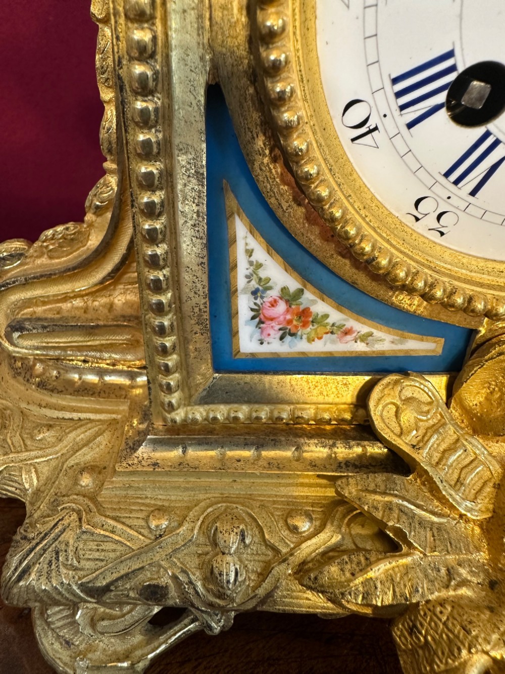 A late 19th-century French gilt bronze mantel clock crowned with a seated cherub figure and featuring an enamel dial with blue porcelain panels. View V