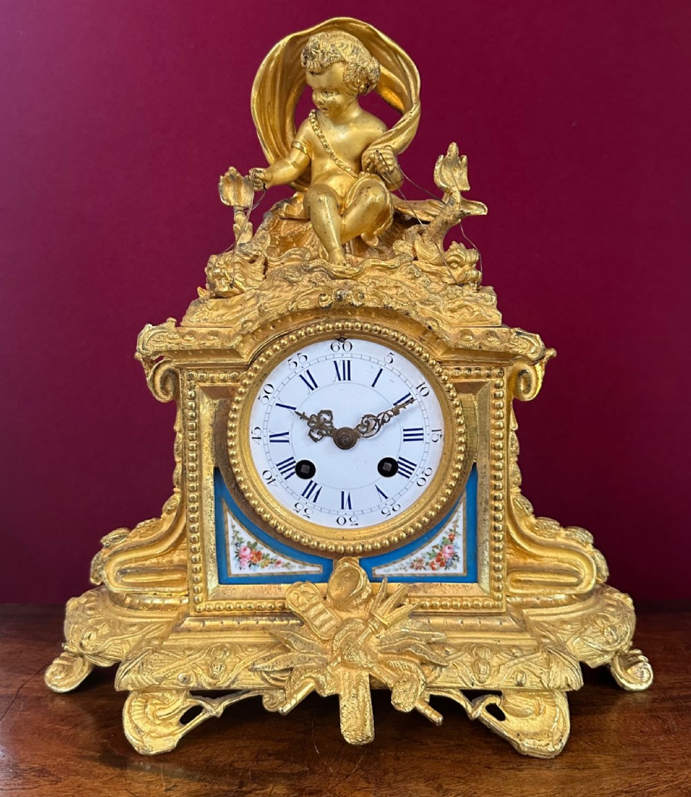 A late 19th-century French gilt bronze mantel clock crowned with a seated cherub figure and featuring an enamel dial with blue porcelain panels. View VI