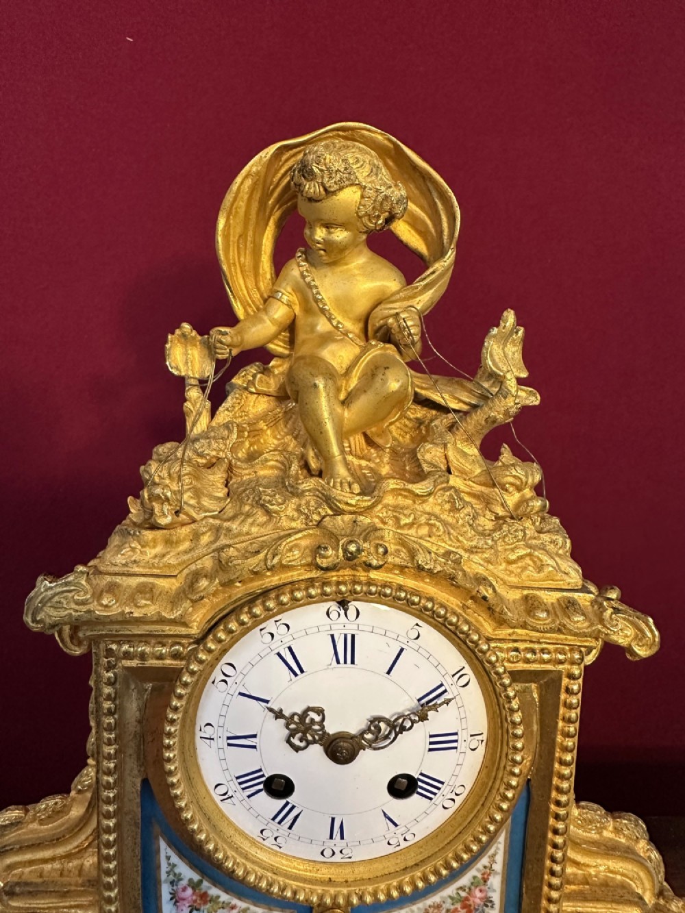 A late 19th-century French gilt bronze mantel clock crowned with a seated cherub figure and featuring an enamel dial with blue porcelain panels. View VII