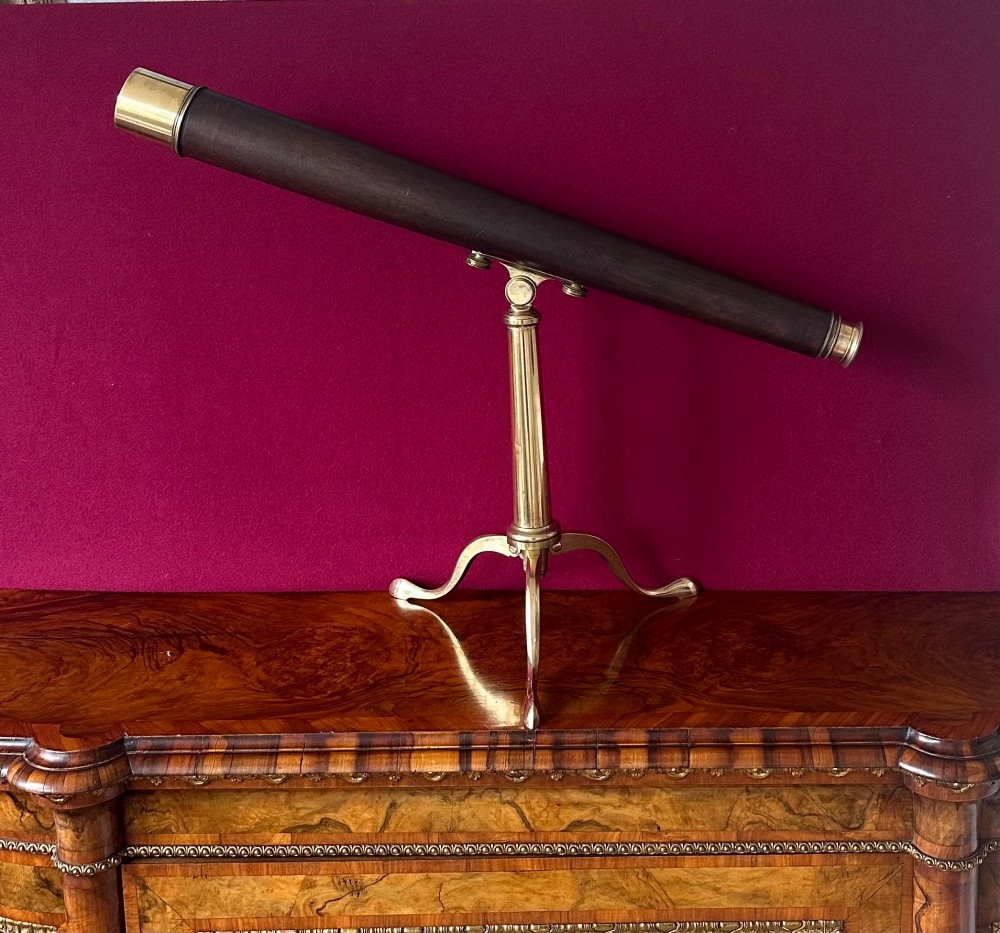 An early nineteenth-century brass tabletop telescope featuring a dark leather barrel casing resting on a brass tripod stand.