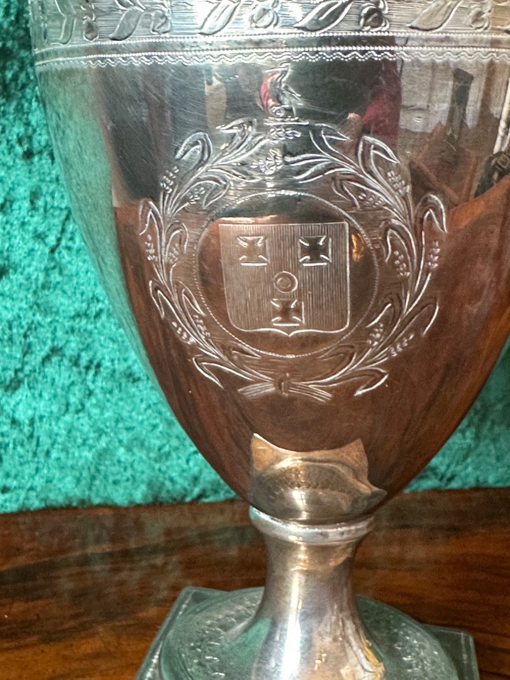 A Georgian silver ewer with an urn-shaped body, engraved heraldic coat of arms, pineapple finial, and a cane-wrapped handle resting on a square base. View II