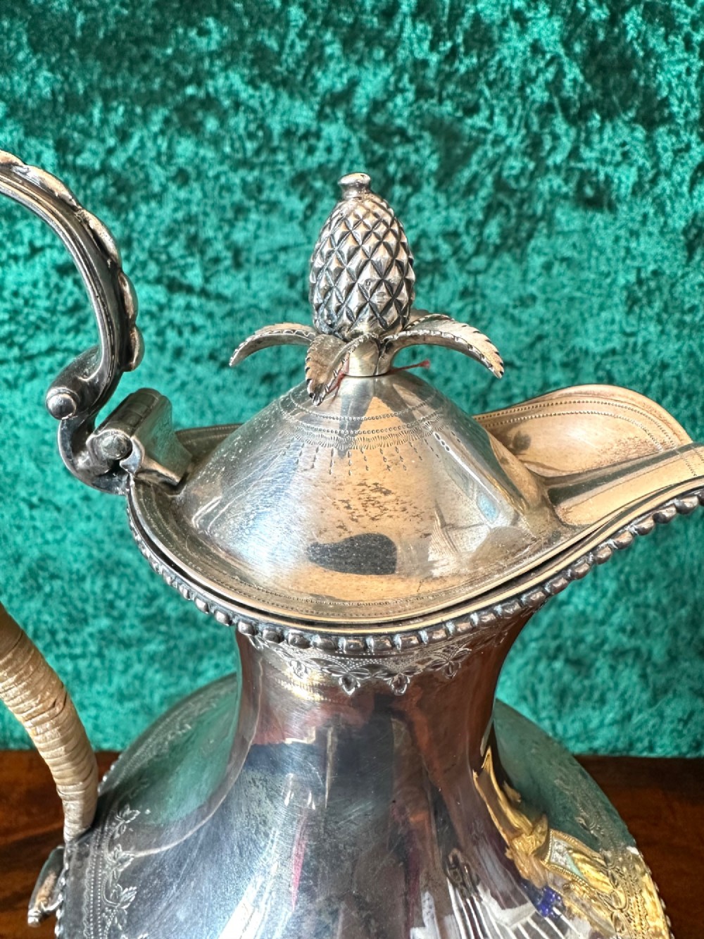 A Georgian silver ewer with an urn-shaped body, engraved heraldic coat of arms, pineapple finial, and a cane-wrapped handle resting on a square base. View III