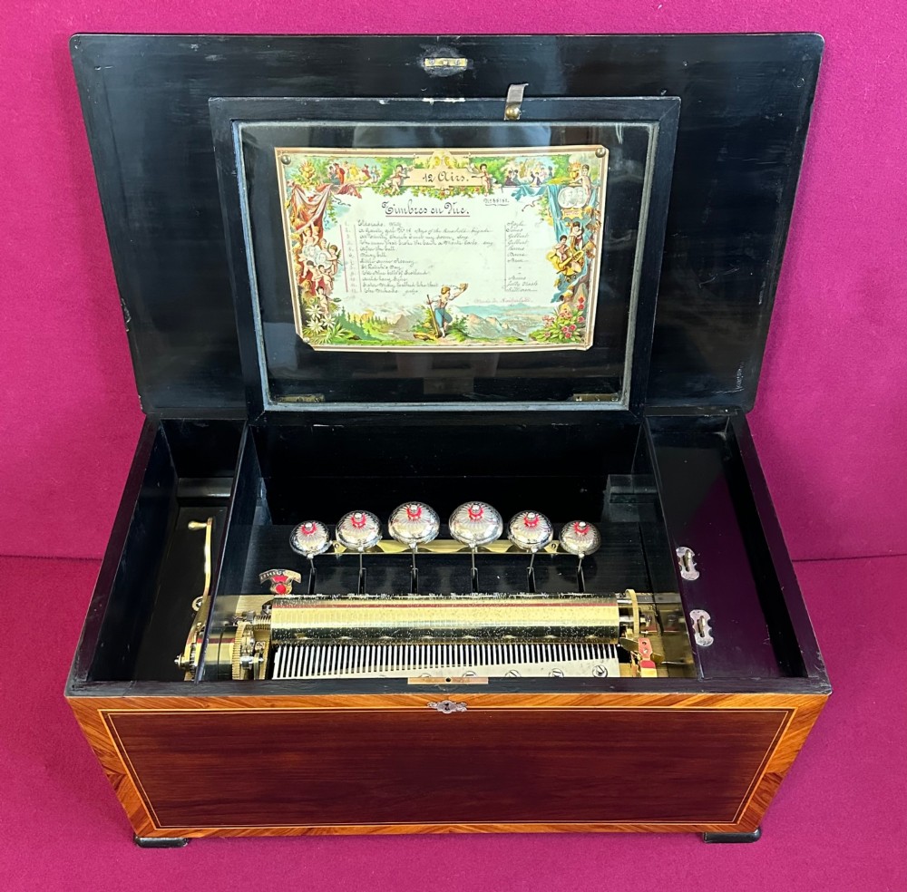 An open Victorian cylinder music box housed in a dark veneered wooden case featuring six exposed bells and an illustrated tune sheet inside the lid.