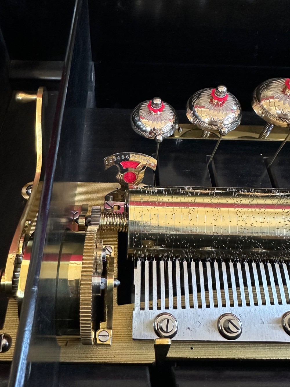 An open Victorian cylinder music box housed in a dark veneered wooden case featuring six exposed bells and an illustrated tune sheet inside the lid. View III