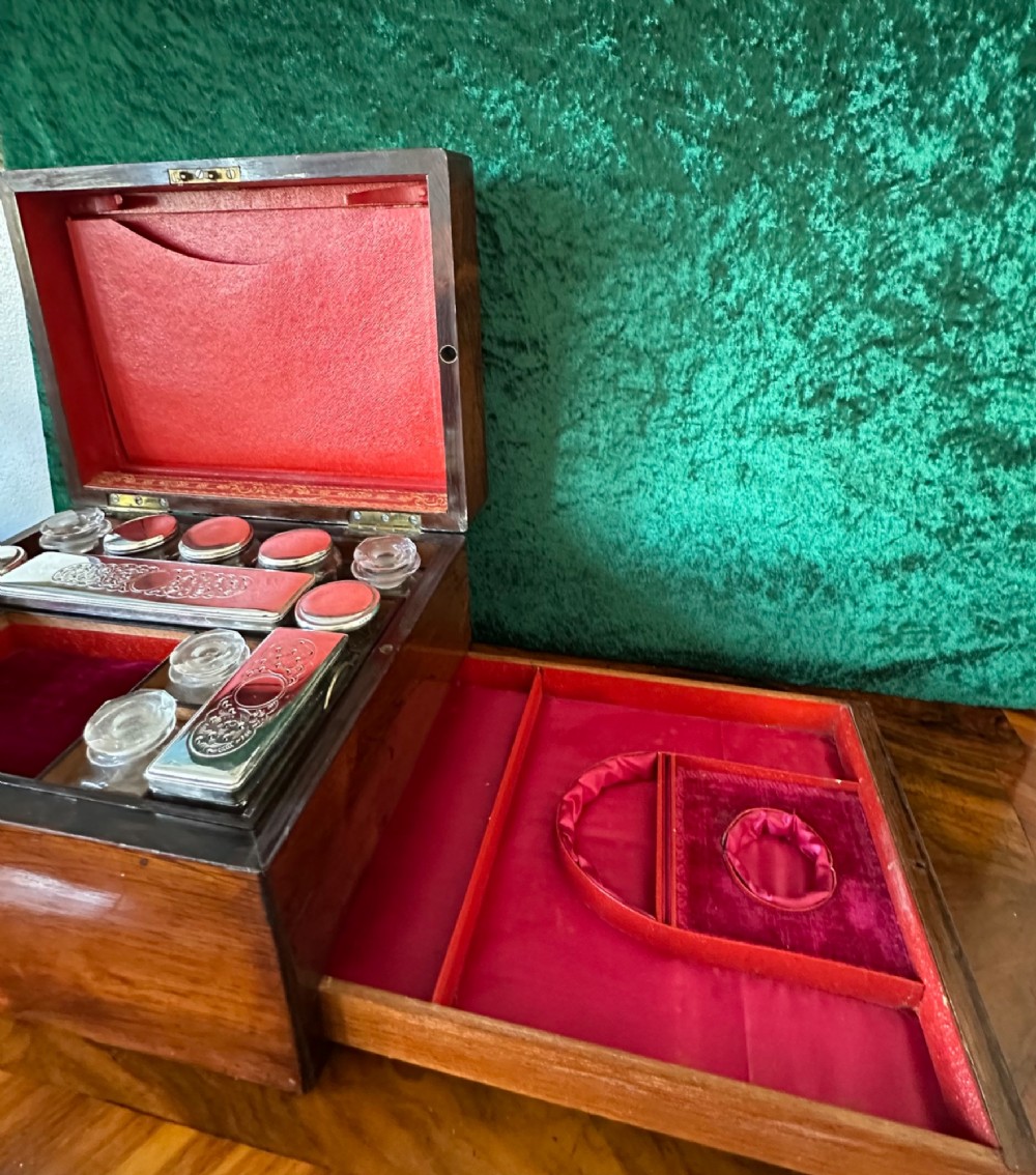 An open Victorian wooden travelling dressing case featuring vibrant red velvet lining, glass toiletry jars, engraved silver lids, and small compartments. View III