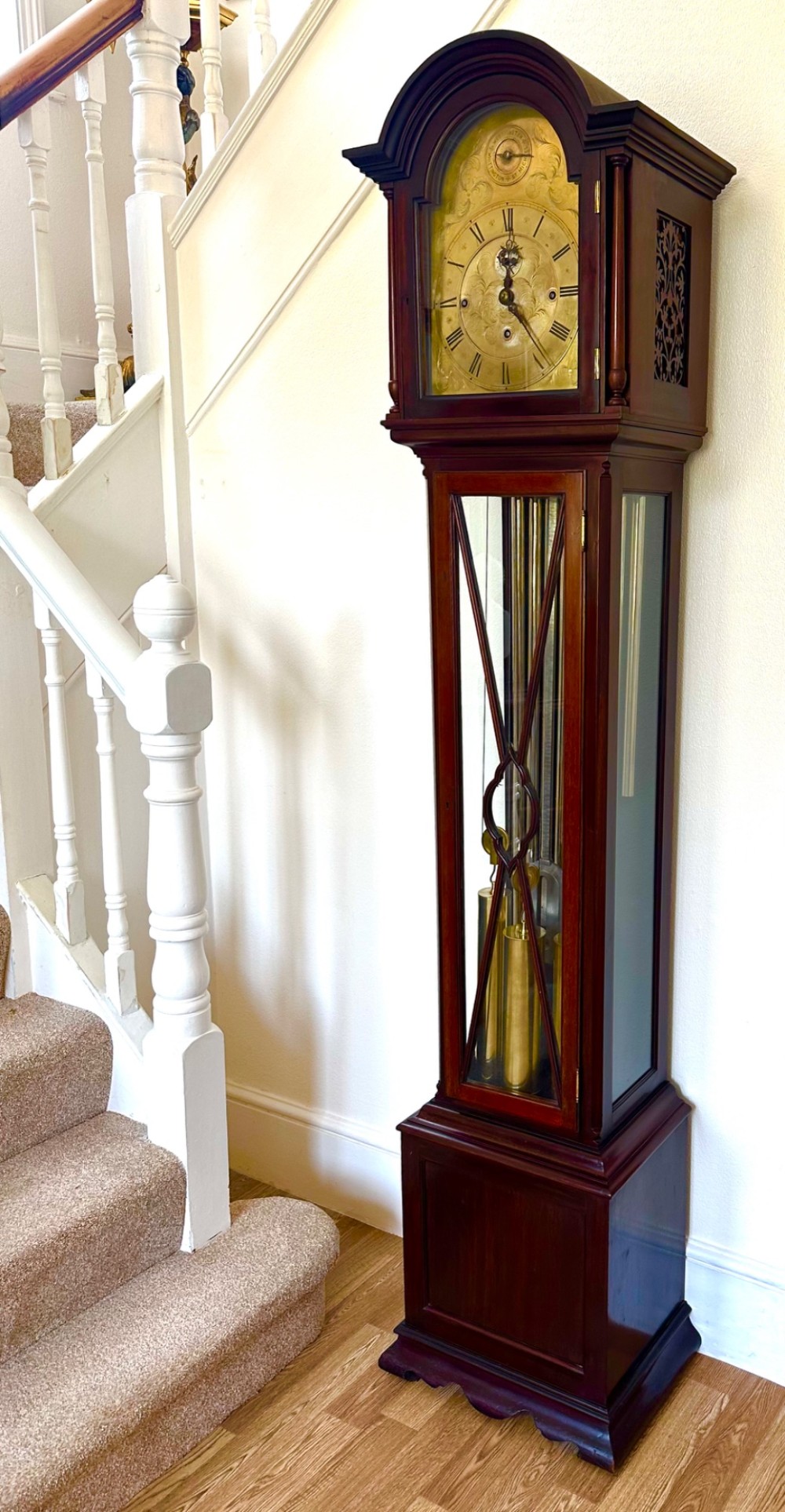 An Edwardian mahogany longcase clock featuring an arched pediment, a brass dial with chime selectors, and a glazed door revealing polished brass weights and tubular bells. View II