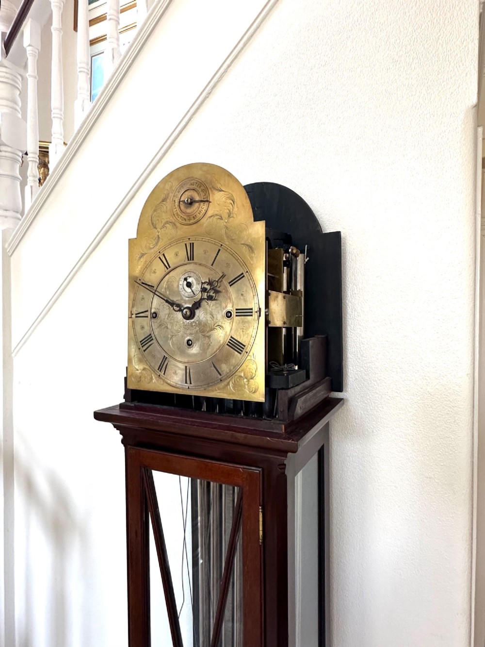 An Edwardian mahogany longcase clock featuring an arched pediment, a brass dial with chime selectors, and a glazed door revealing polished brass weights and tubular bells. View V