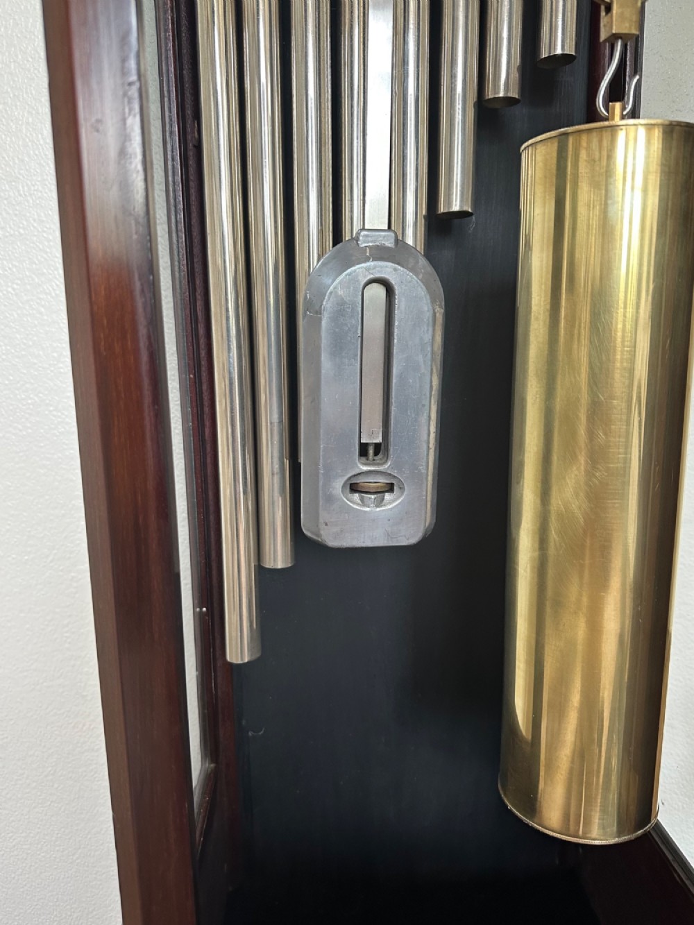 An Edwardian mahogany longcase clock featuring an arched pediment, a brass dial with chime selectors, and a glazed door revealing polished brass weights and tubular bells. View VI
