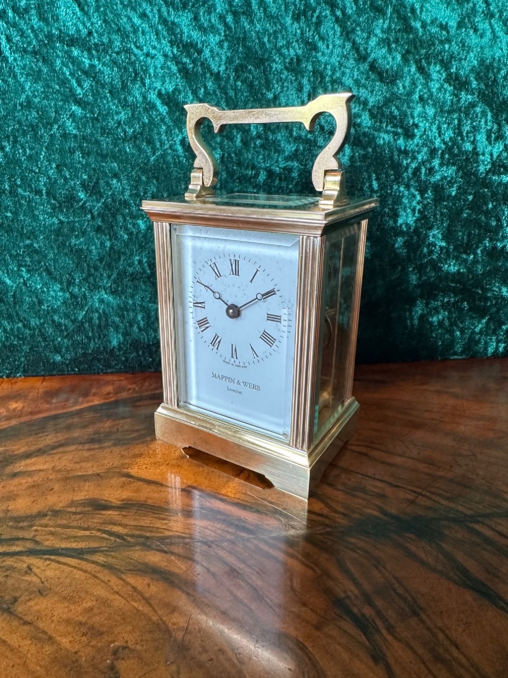 A rectangular brass carriage clock featuring bevelled glass side panels, a top handle, and a white enamel dial with Roman numerals marked Mappin & Webb London.