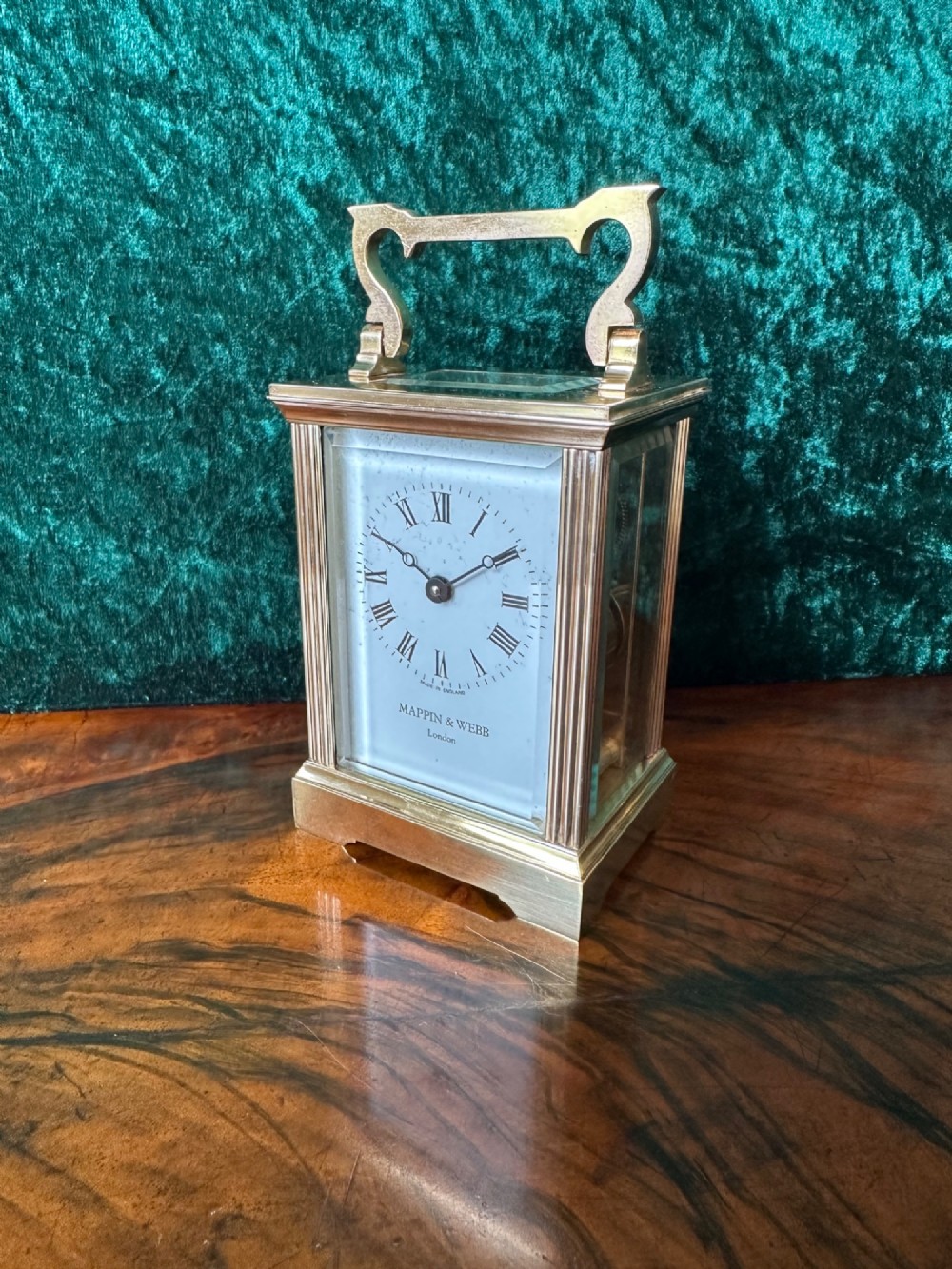 A rectangular brass carriage clock featuring bevelled glass side panels, a top handle, and a white enamel dial with Roman numerals marked Mappin & Webb London. View VI