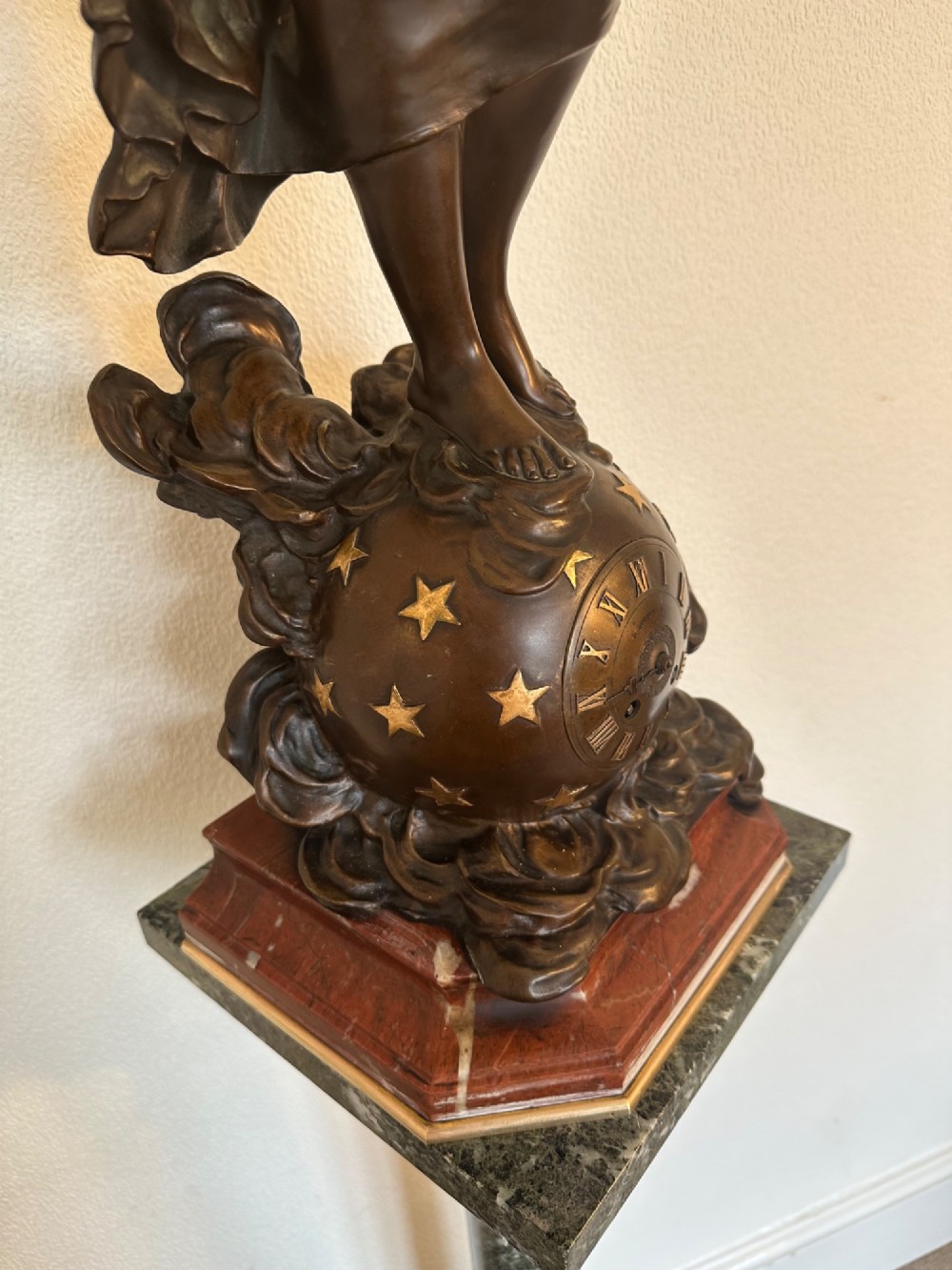 A dark bronze sculpture depicting a draped female figure standing atop a starry globe and mounted on a dark red marble base. View II