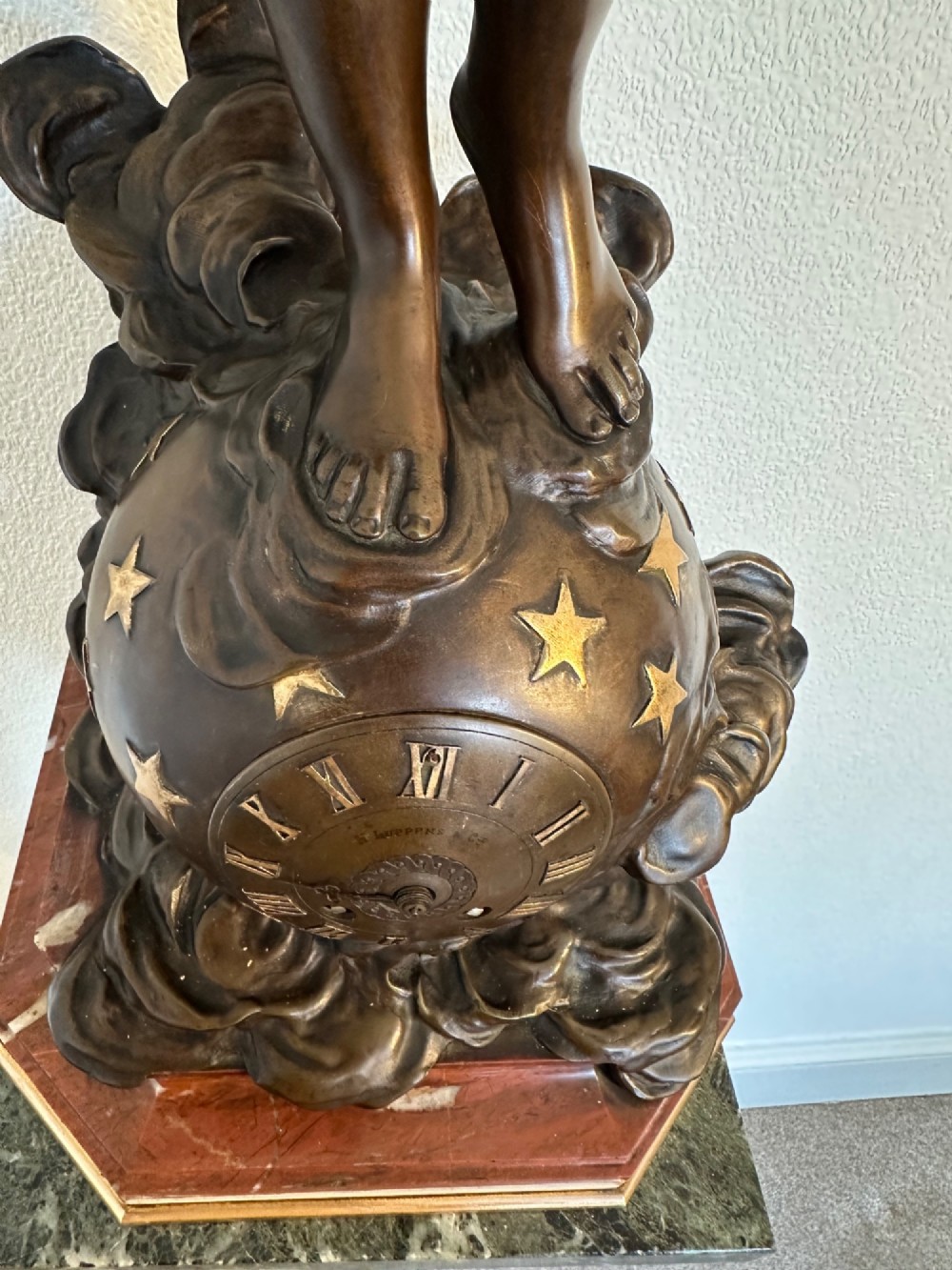 A dark bronze sculpture depicting a draped female figure standing atop a starry globe and mounted on a dark red marble base. View VI