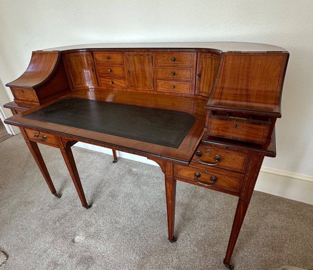 An Edwardian satinwood Carlton House desk featuring a leather writing surface, curved drawer superstructure, and square tapered legs on castors.