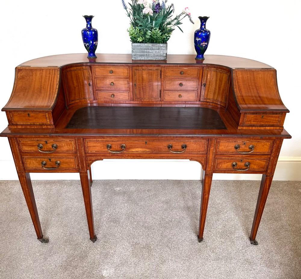 An Edwardian satinwood Carlton House desk featuring a leather writing surface, curved drawer superstructure, and square tapered legs on castors. View II