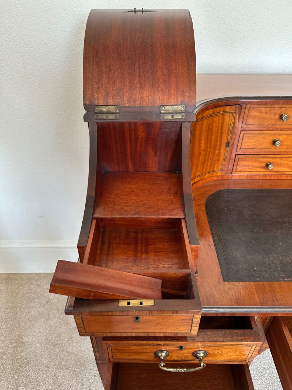 An Edwardian satinwood Carlton House desk featuring a leather writing surface, curved drawer superstructure, and square tapered legs on castors. View III
