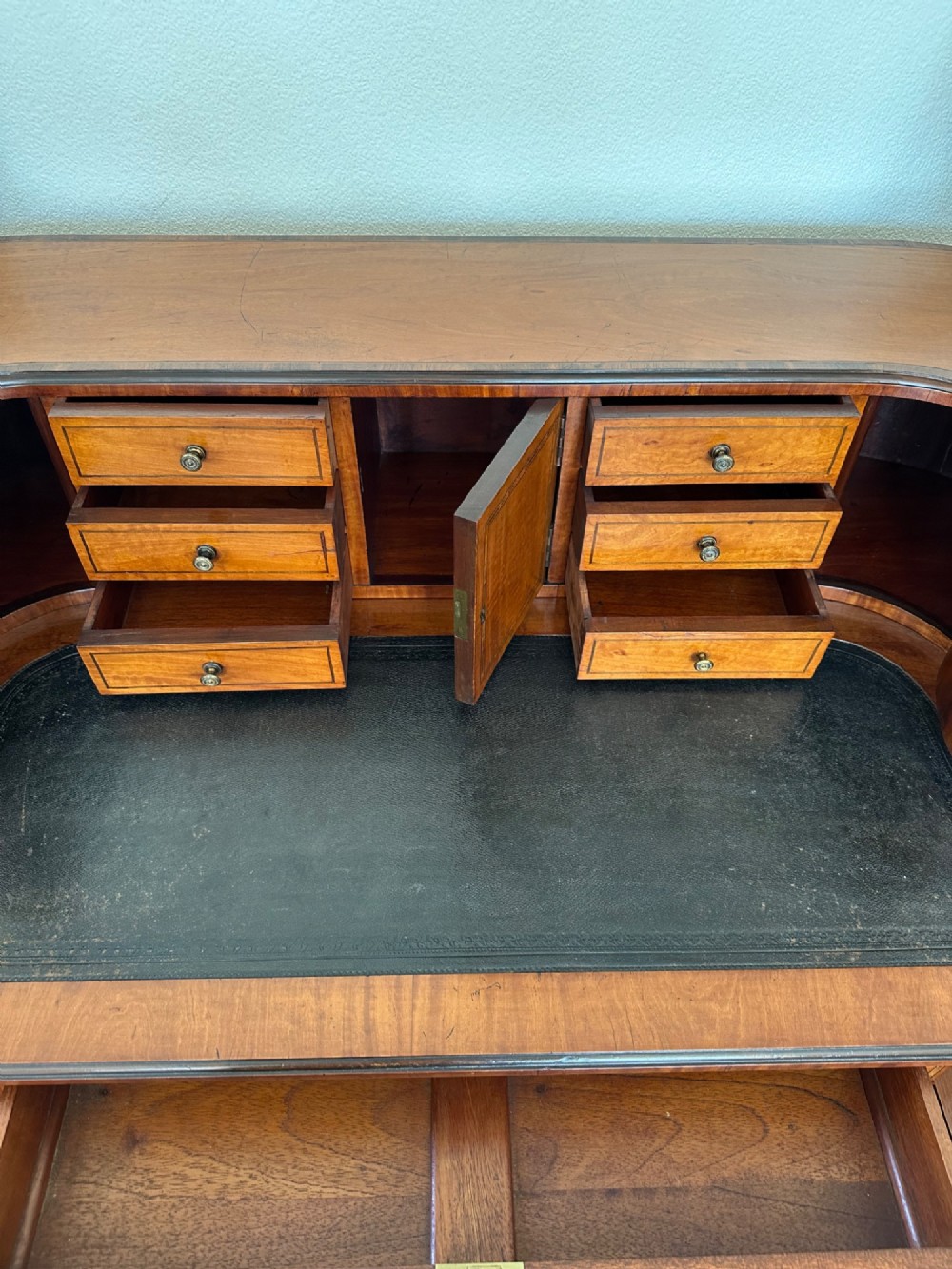 An Edwardian satinwood Carlton House desk featuring a leather writing surface, curved drawer superstructure, and square tapered legs on castors. View IV
