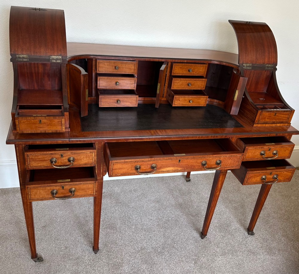 An Edwardian satinwood Carlton House desk featuring a leather writing surface, curved drawer superstructure, and square tapered legs on castors. View V