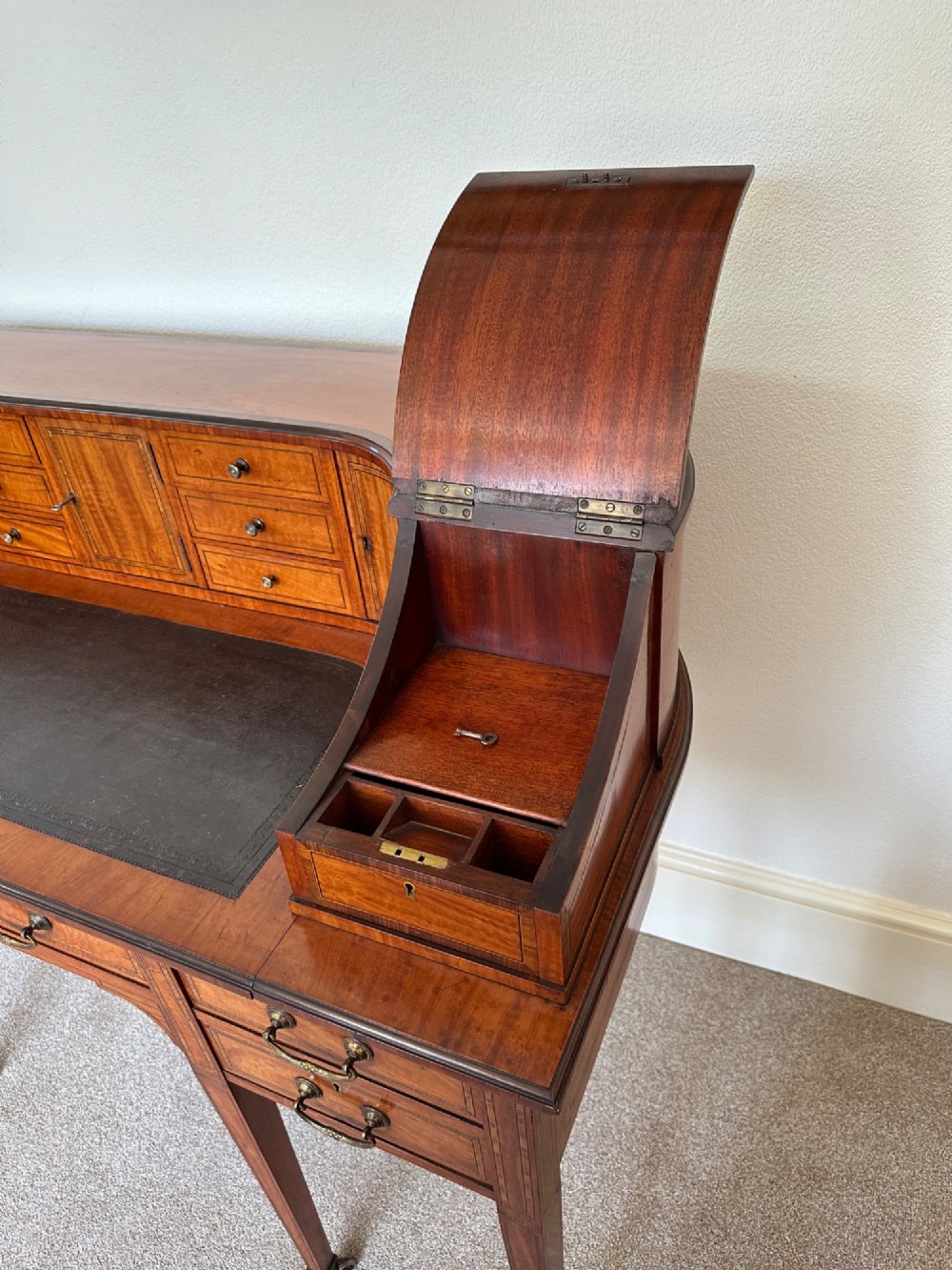 An Edwardian satinwood Carlton House desk featuring a leather writing surface, curved drawer superstructure, and square tapered legs on castors. View VI