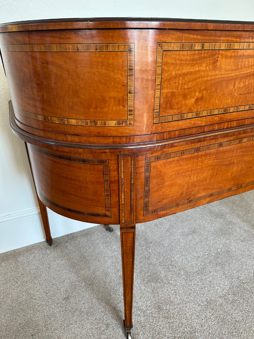 An Edwardian satinwood Carlton House desk featuring a leather writing surface, curved drawer superstructure, and square tapered legs on castors. View VIII