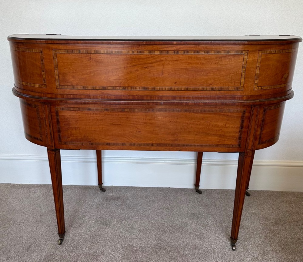 An Edwardian satinwood Carlton House desk featuring a leather writing surface, curved drawer superstructure, and square tapered legs on castors. View IX