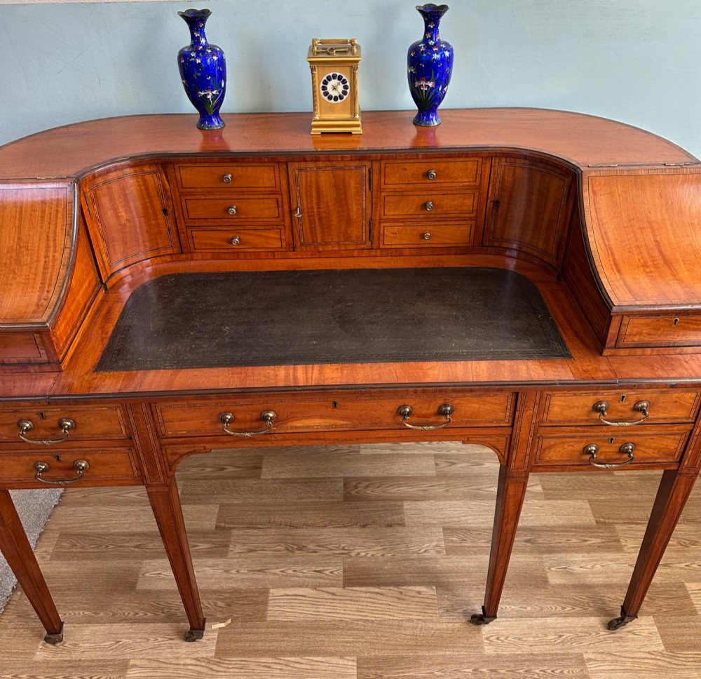 An Edwardian satinwood Carlton House desk featuring a leather writing surface, curved drawer superstructure, and square tapered legs on castors. View X