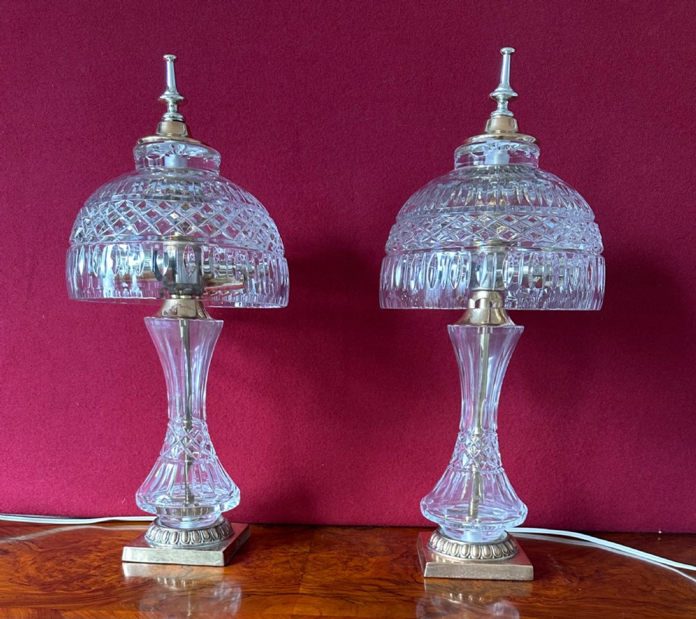 A pair of matching cut crystal table lamps featuring dome shades, faceted baluster stems, square metal bases, and pointed finials.