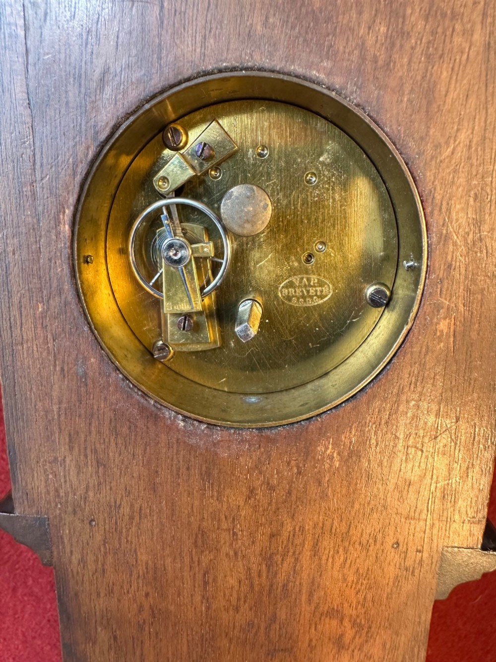 A wooden miniature grandfather clock featuring brass foliate inlay, an arched hood with three turned finials, black side columns, and a cream dial face with Roman numerals. View VI