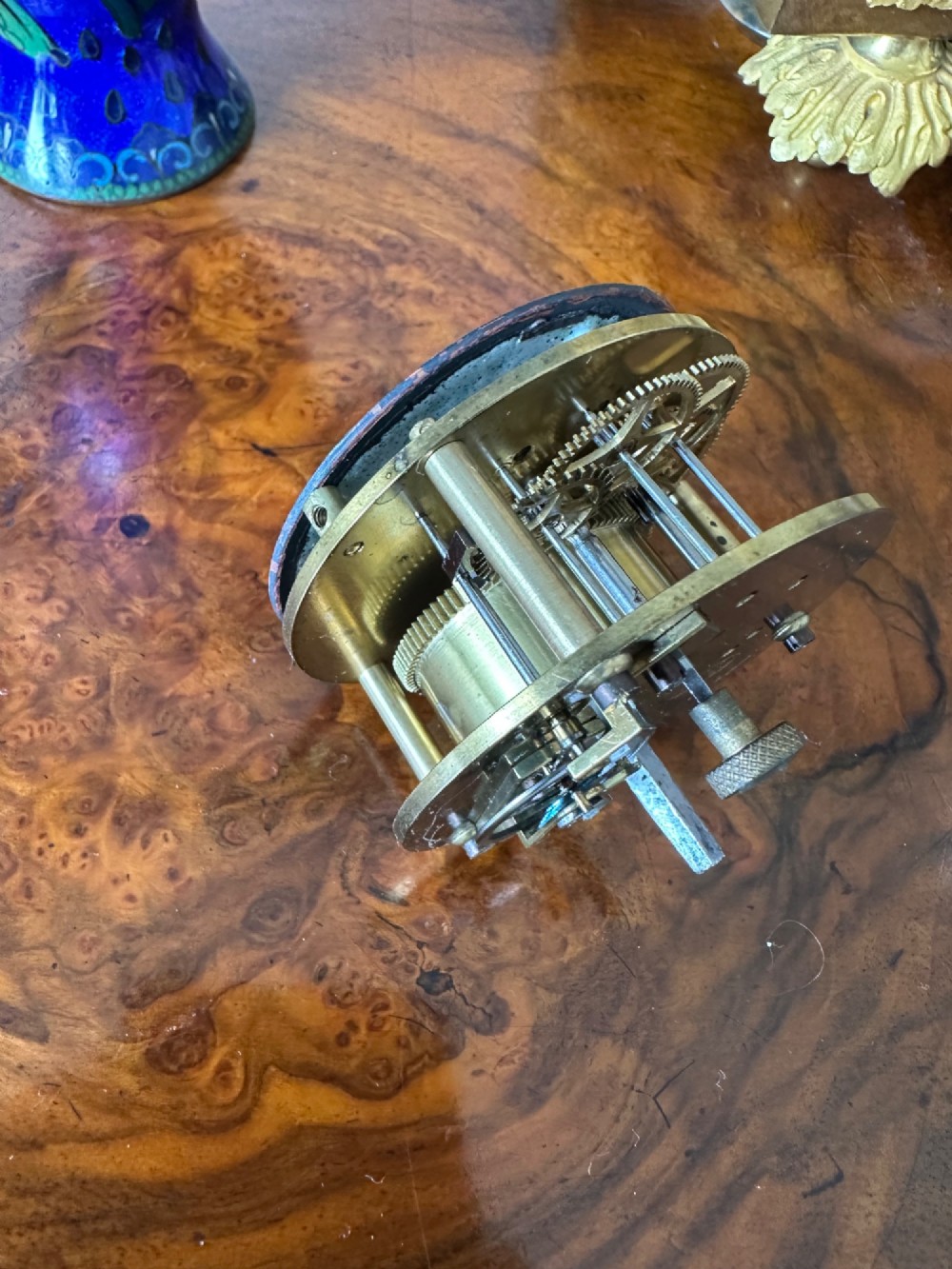 A wooden miniature grandfather clock featuring brass foliate inlay, an arched hood with three turned finials, black side columns, and a cream dial face with Roman numerals. View VIII