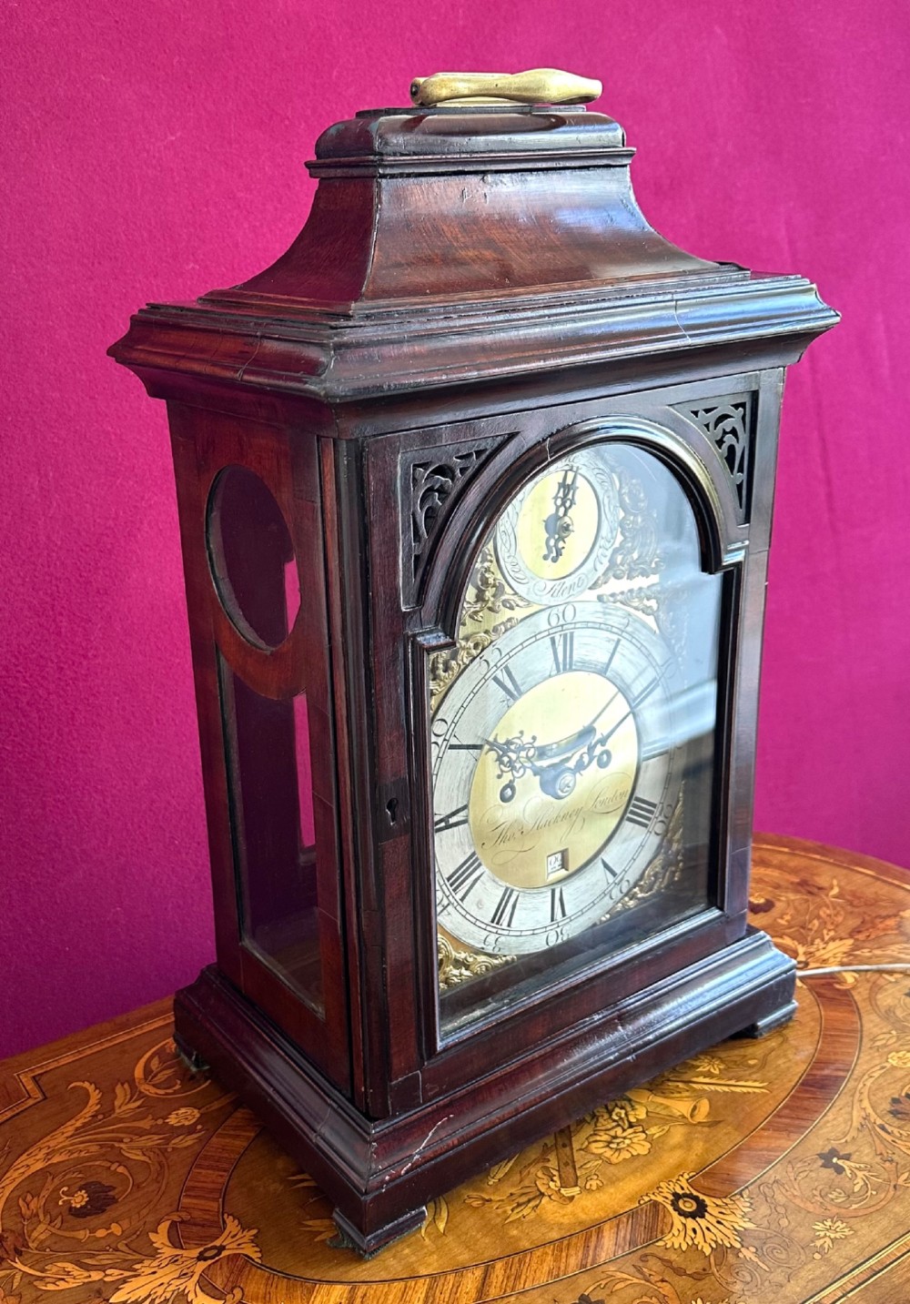 A mid-18th-century Georgian mahogany bracket clock featuring an upper brass carrying handle, an arched glass front door, and an engraved brass dial with a silvered chapter ring. View IV
