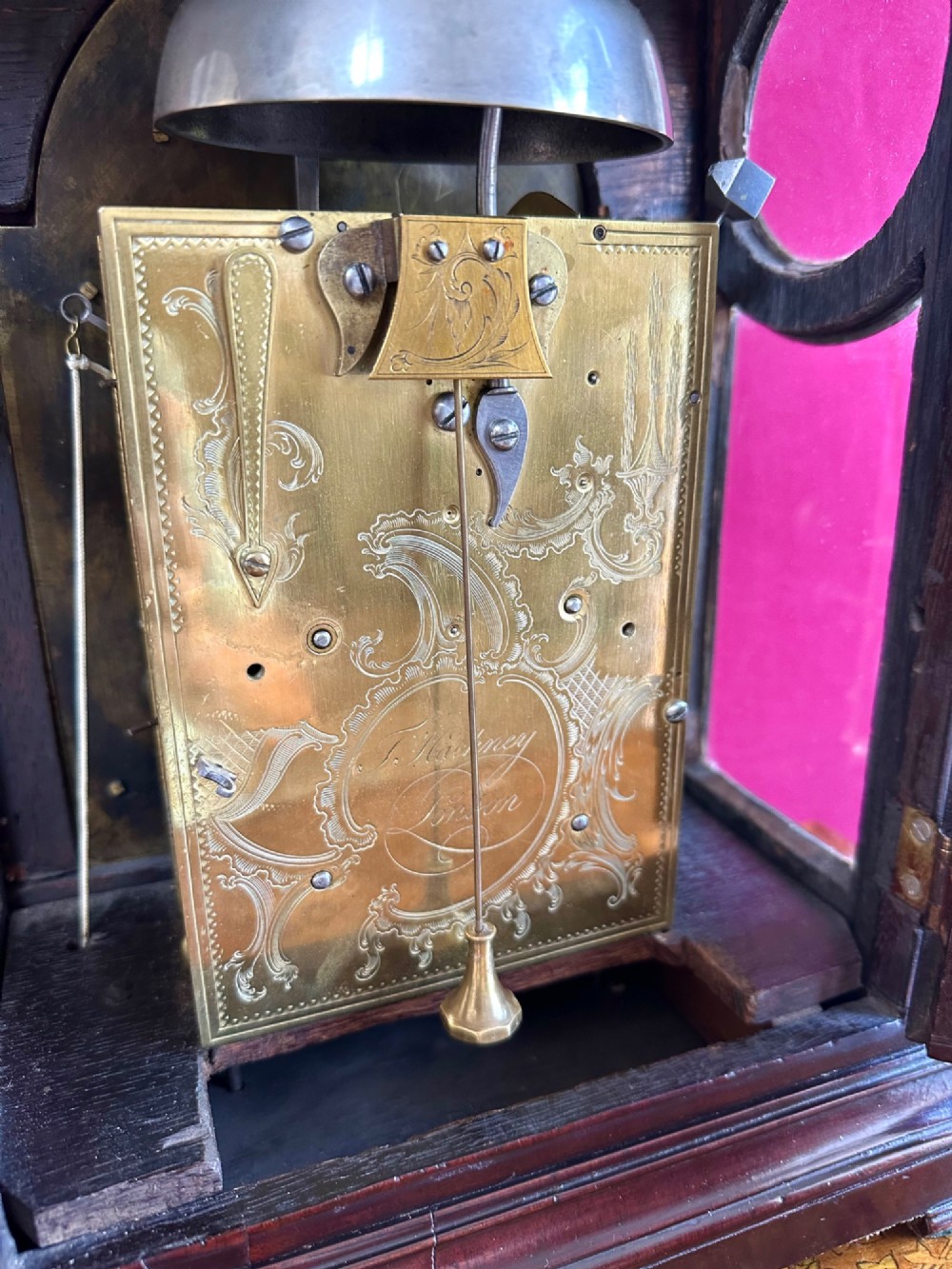 A mid-18th-century Georgian mahogany bracket clock featuring an upper brass carrying handle, an arched glass front door, and an engraved brass dial with a silvered chapter ring. View V