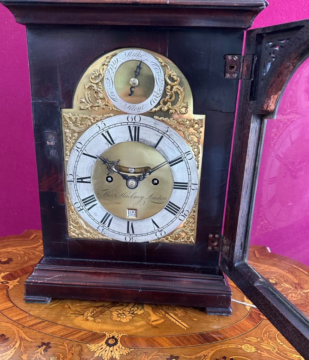 A mid-18th-century Georgian mahogany bracket clock featuring an upper brass carrying handle, an arched glass front door, and an engraved brass dial with a silvered chapter ring. View XII