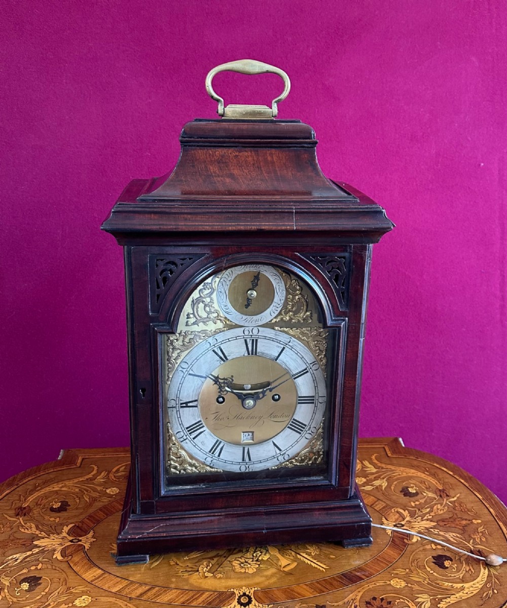 A mid-18th-century Georgian mahogany bracket clock featuring an upper brass carrying handle, an arched glass front door, and an engraved brass dial with a silvered chapter ring. View XV