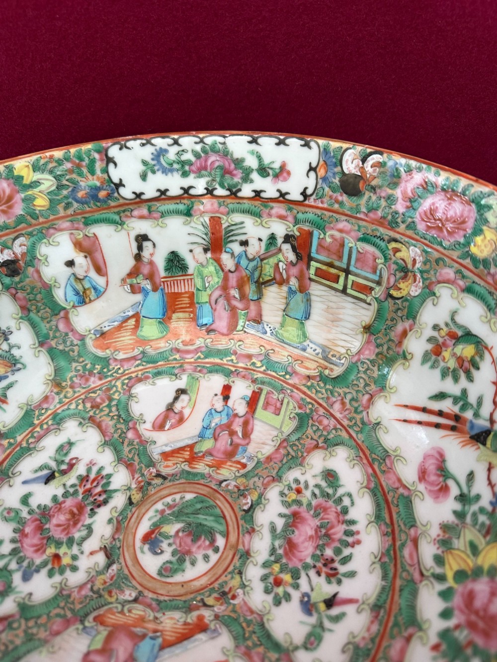 A circular Chinese export porcelain bowl featuring hand-painted panels with human figures in courtly attire framed by floral borders. View V