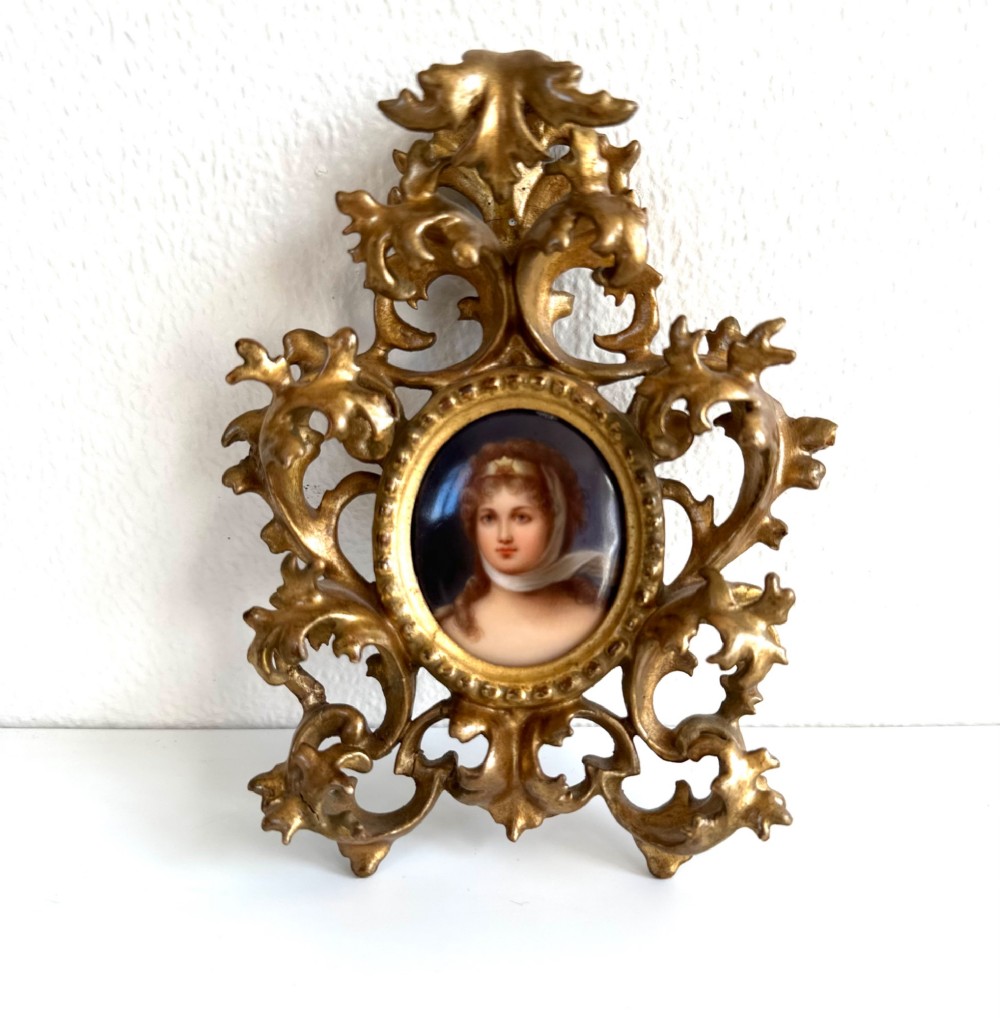 A late 19th-century oval miniature portrait of a woman set within an elaborate gilt metal frame featuring acanthus scrollwork and pierced details.
