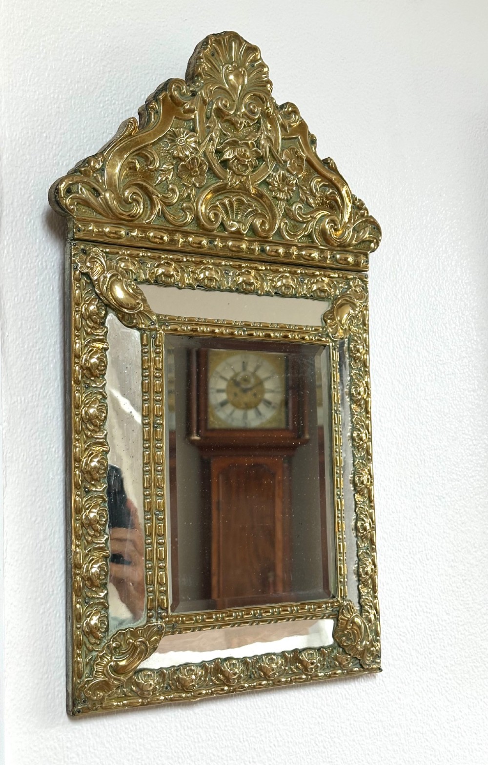 An antique repousse brass marginal mirror featuring an ornate floral pediment crest and bevelled glass borders. View V