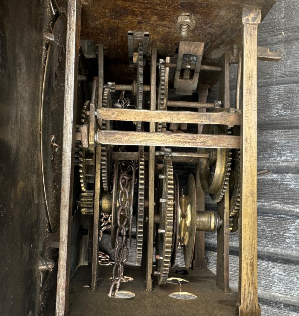 A square eighteenth-century brass clock dial with cast corner spandrels, Roman numerals, engraved centre detailing, and rusty iron chains. View V