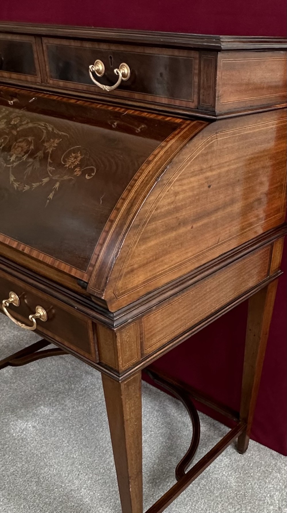 An Edwardian mahogany cylinder bureau featuring floral marquetry inlay on the curved front, brass handles, square tapered legs, and crossbanded borders. View III
