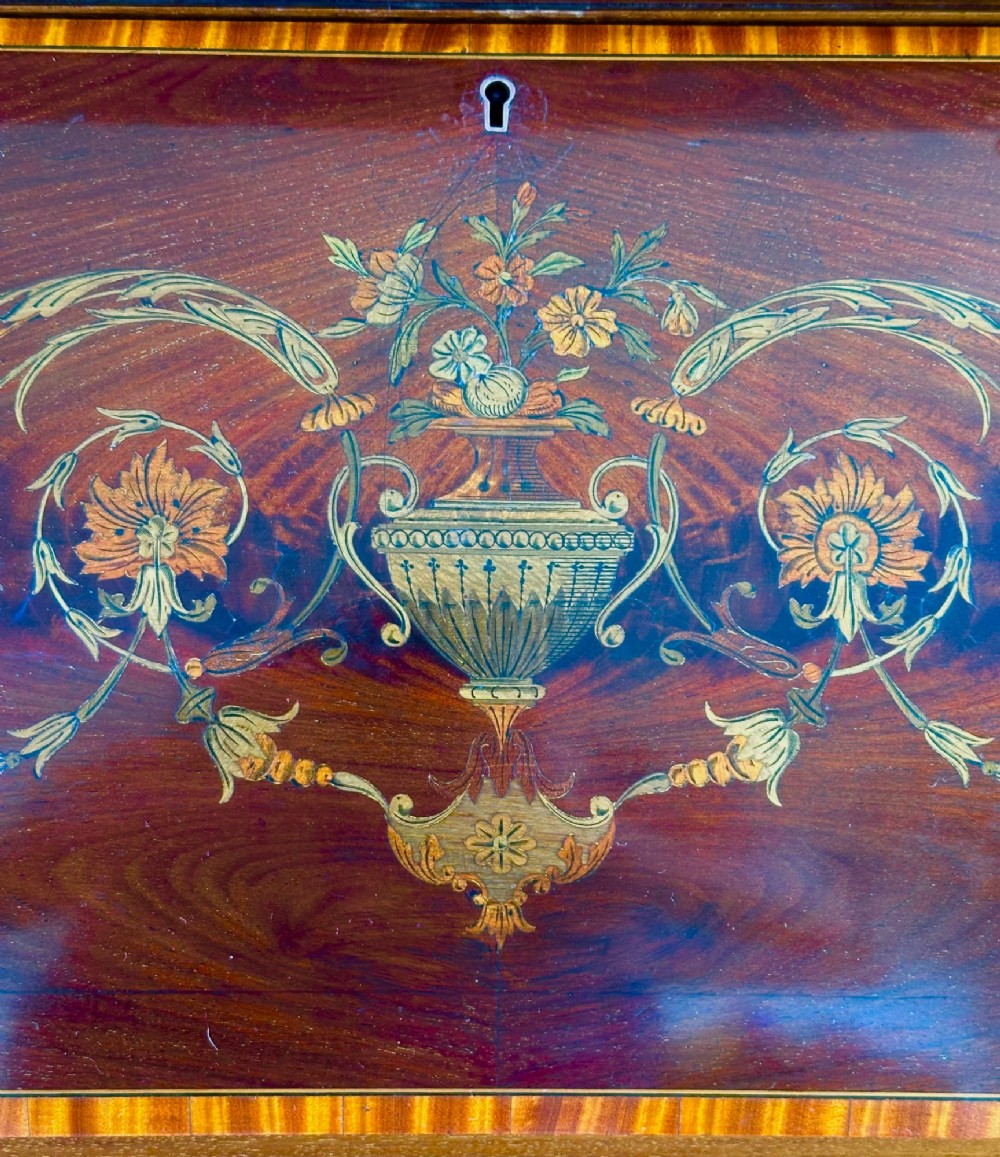 An Edwardian mahogany cylinder bureau featuring floral marquetry inlay on the curved front, brass handles, square tapered legs, and crossbanded borders. View V