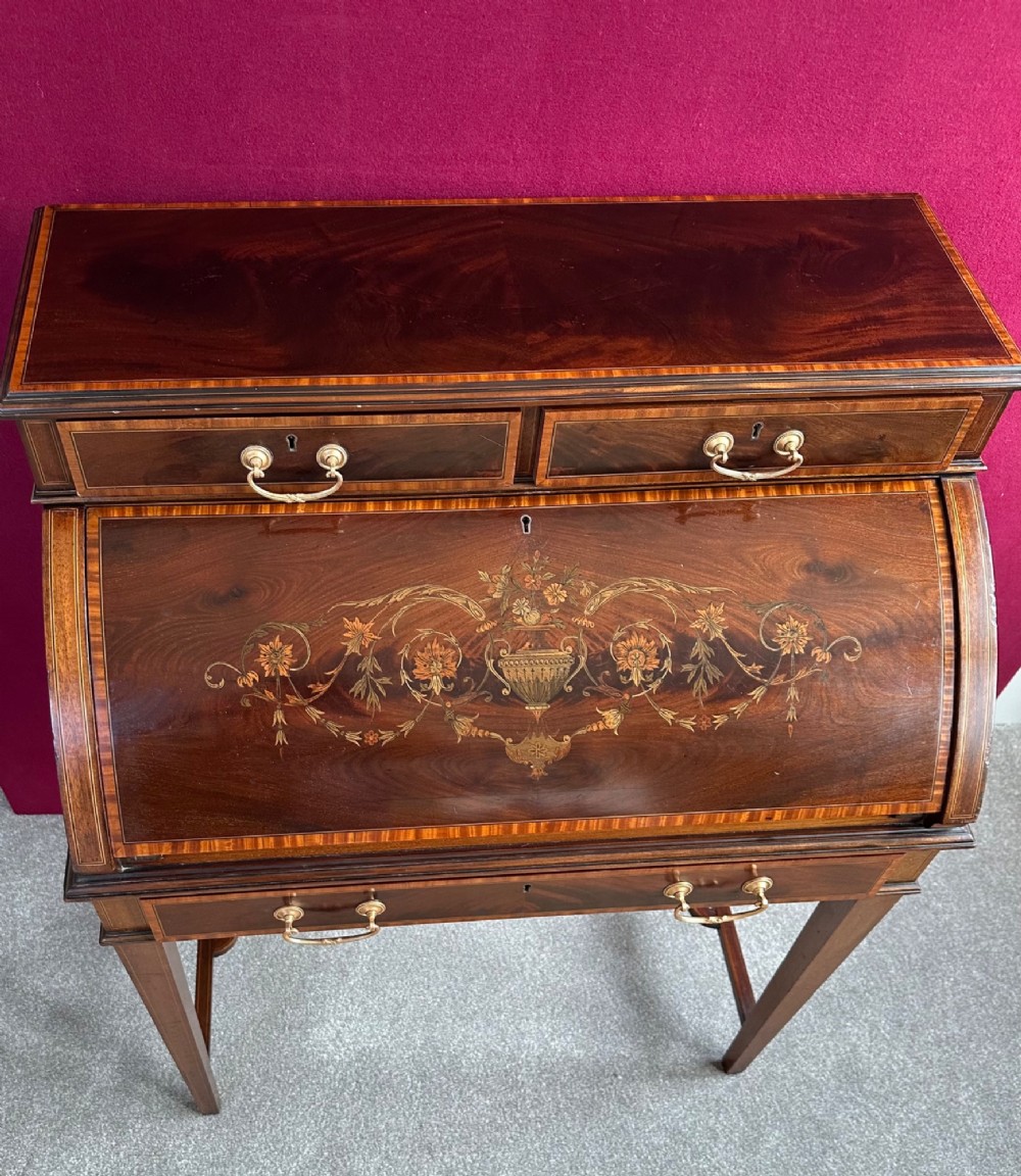 An Edwardian mahogany cylinder bureau featuring floral marquetry inlay on the curved front, brass handles, square tapered legs, and crossbanded borders. View VI