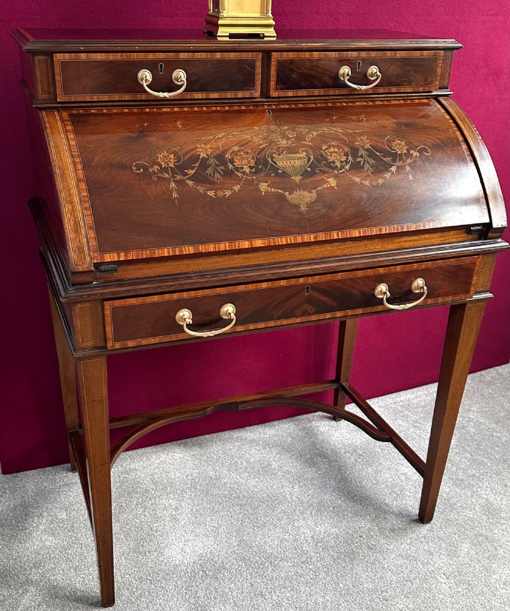 An Edwardian mahogany cylinder bureau featuring floral marquetry inlay on the curved front, brass handles, square tapered legs, and crossbanded borders. View VII