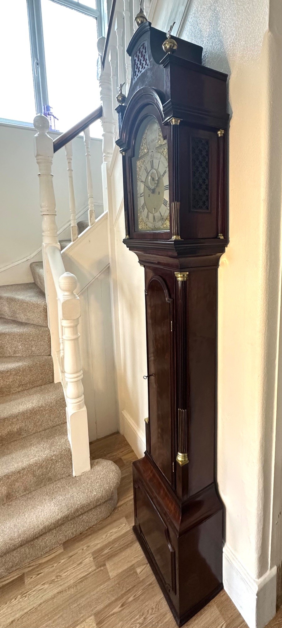 A tall Georgian mahogany longcase clock featuring brass eagle finials, a swan-neck pediment, fluted columns, and an engraved brass dial. View IX