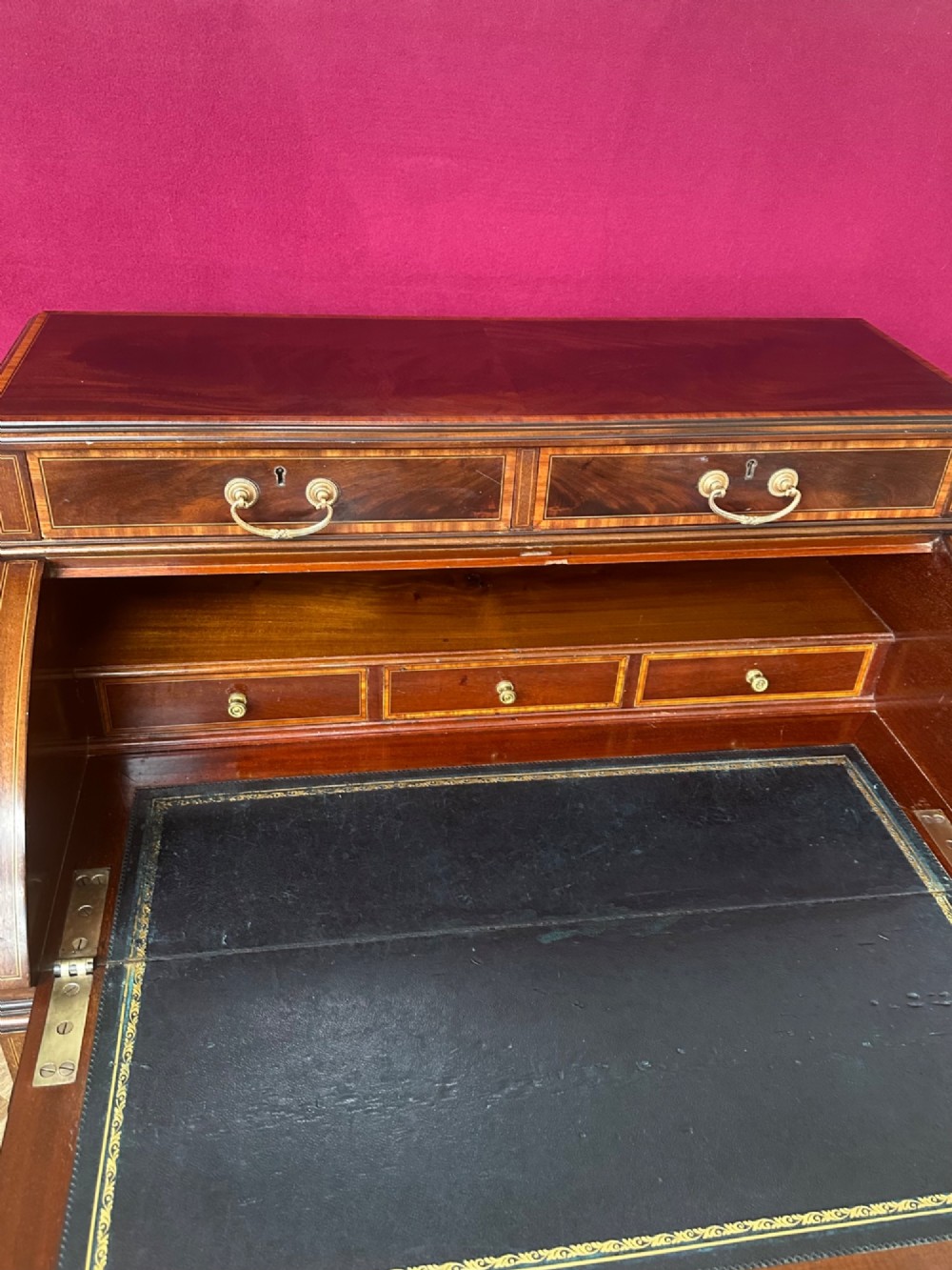 An Edwardian mahogany cylinder bureau featuring floral marquetry inlay on the curved front, brass handles, square tapered legs, and crossbanded borders. View X
