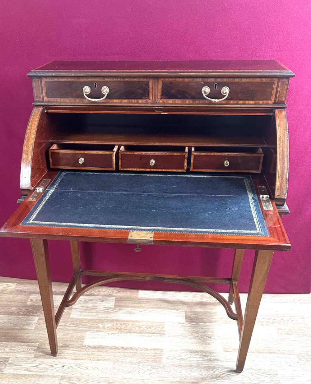An Edwardian mahogany cylinder bureau featuring floral marquetry inlay on the curved front, brass handles, square tapered legs, and crossbanded borders. View XI