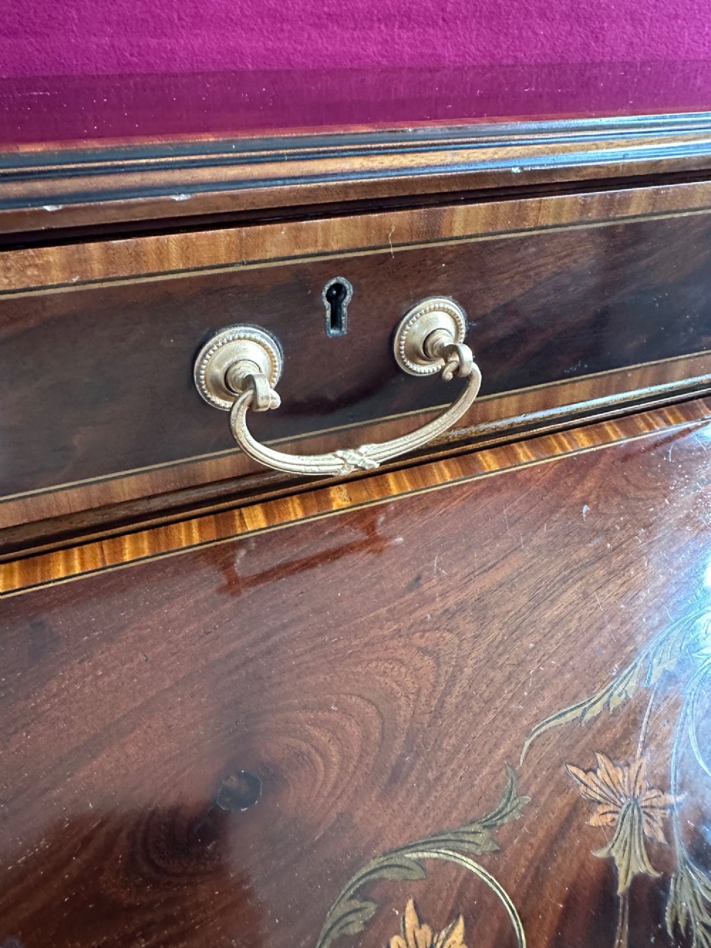 An Edwardian mahogany cylinder bureau featuring floral marquetry inlay on the curved front, brass handles, square tapered legs, and crossbanded borders. View XII