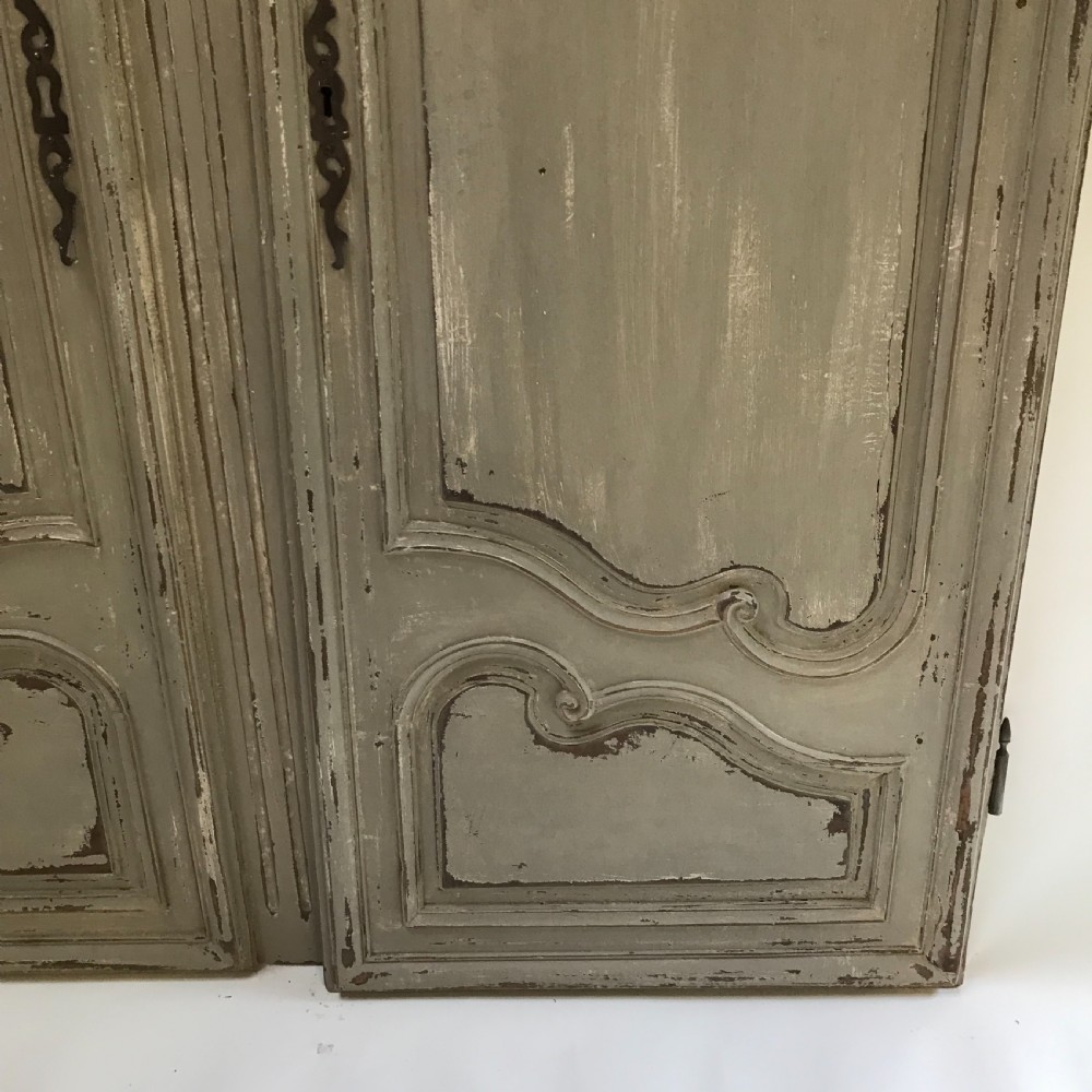 A pair of grey painted wooden doors featuring carved Louis XV style moulded panels and a distressed paint finish with central iron escutcheons. View IV