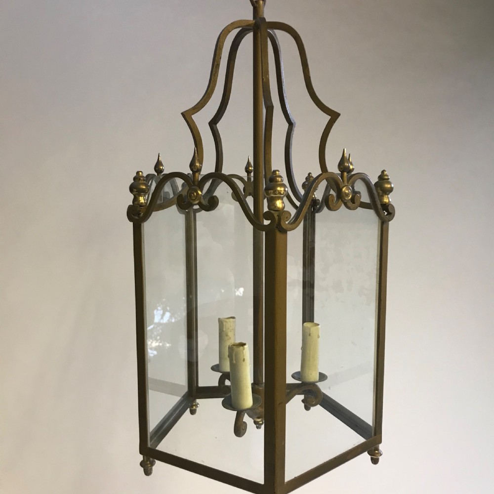 A large French brass hall lantern with clear glass side panels, a scrolled metal crown, finials, and a four-light central fitting.