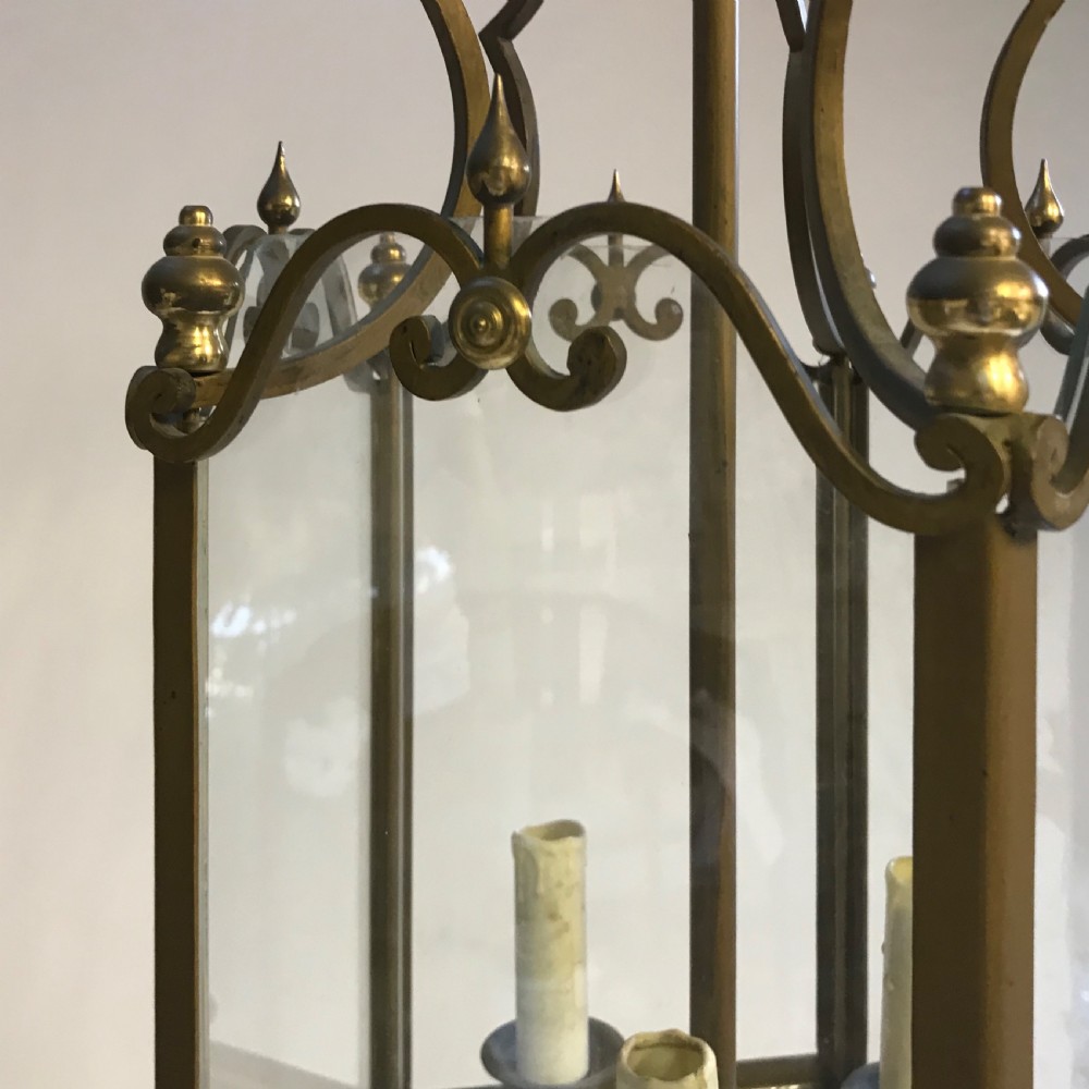 A large French brass hall lantern with clear glass side panels, a scrolled metal crown, finials, and a four-light central fitting. View II