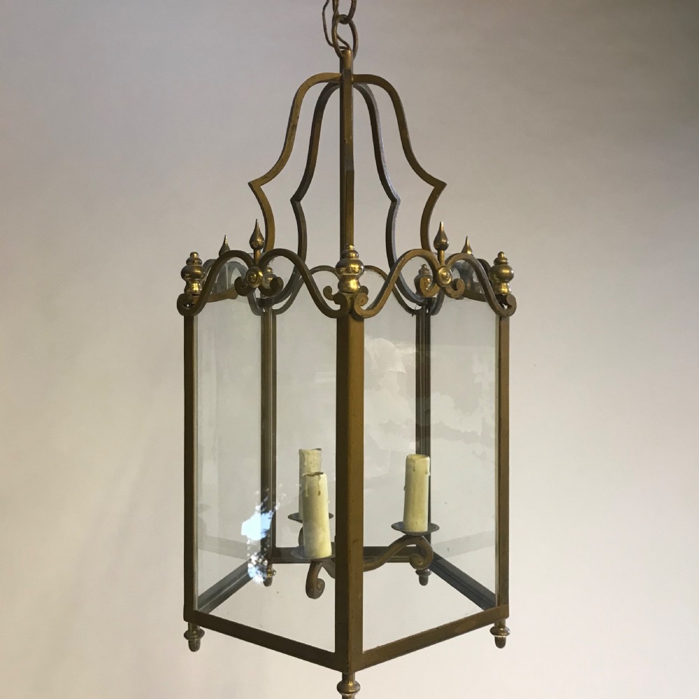 A large French brass hall lantern with clear glass side panels, a scrolled metal crown, finials, and a four-light central fitting. View III